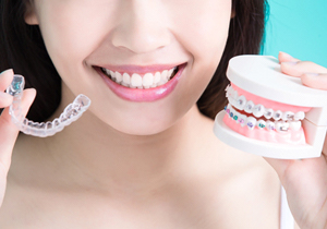 A woman holding a clear aligner tray in one hand and metal braces in the other