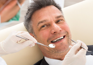 A smiling man is getting a gum exam from a dentist 